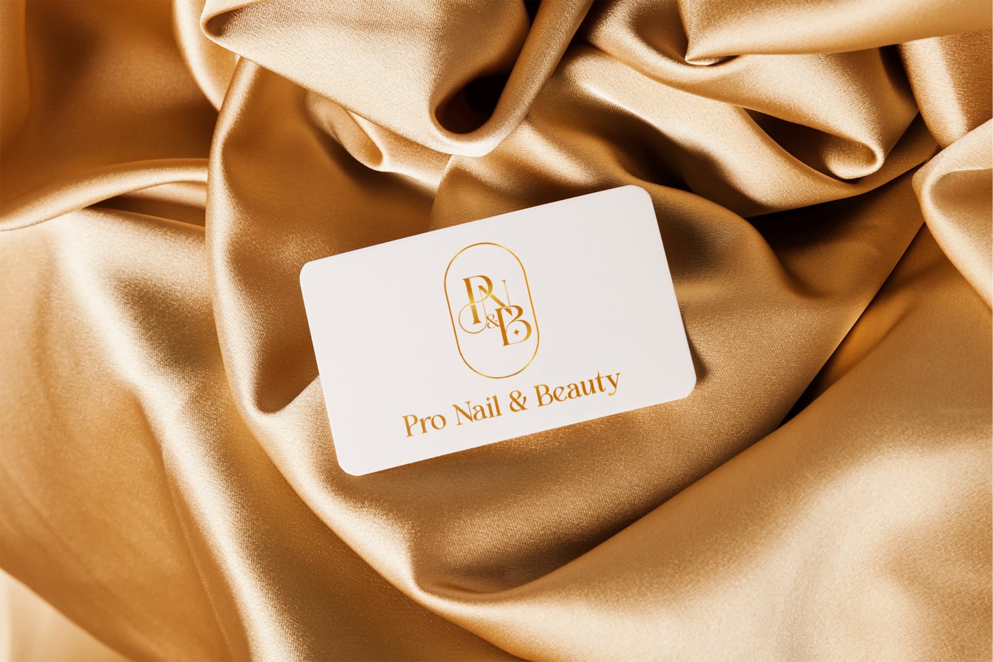 The Pro Nails & Beauty business card, gold monogram on white, photographed on gold satin
