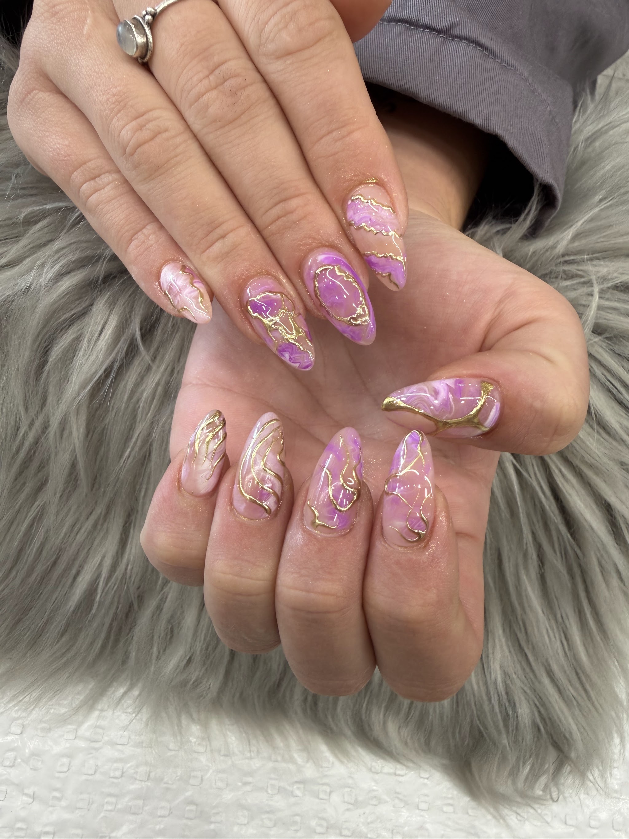 Lilac marble effect nail art with gold foil accents on almond shaped nails