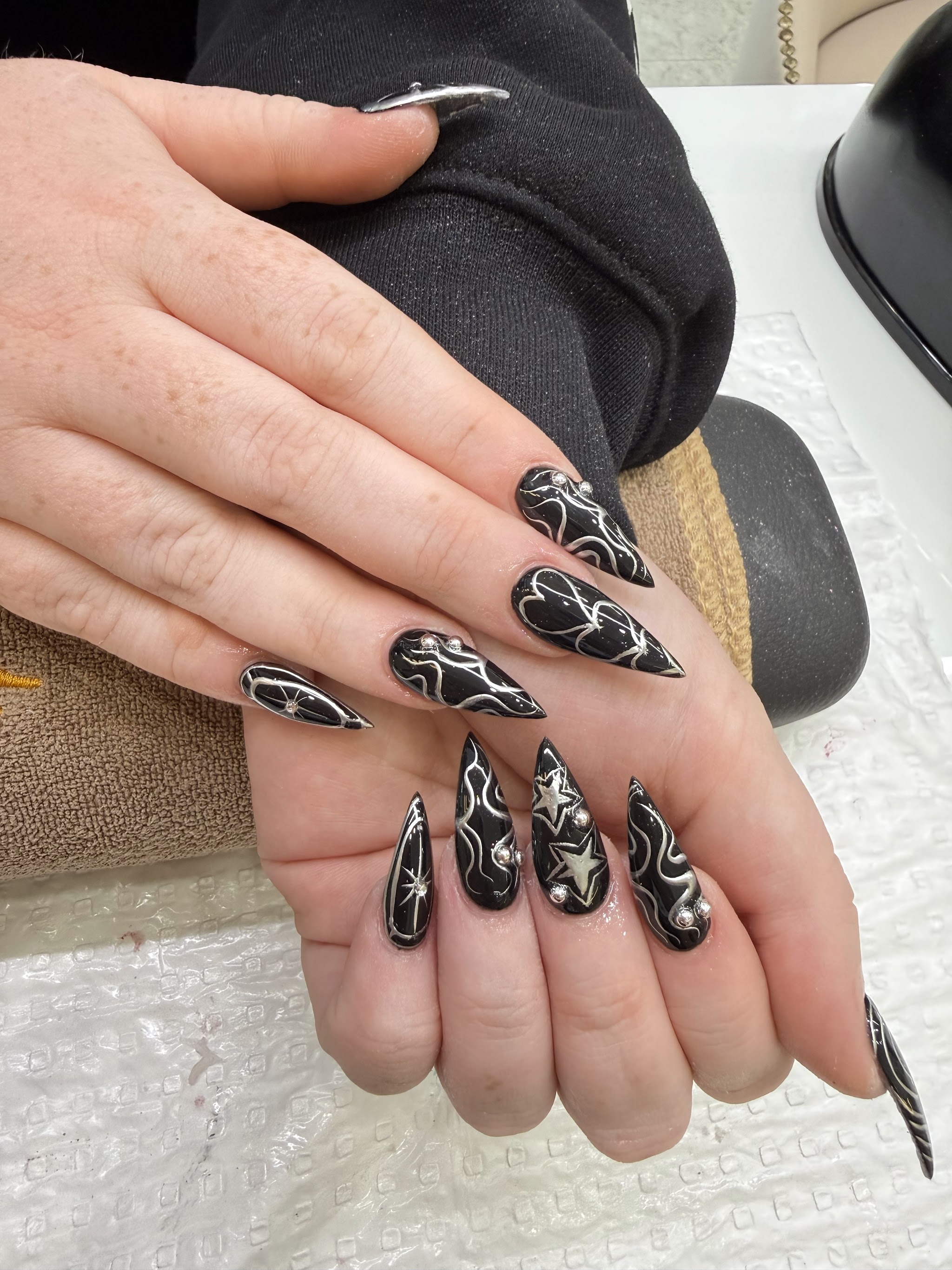 Black and silver stiletto nail art with swirl linework, star motifs and gem accents
